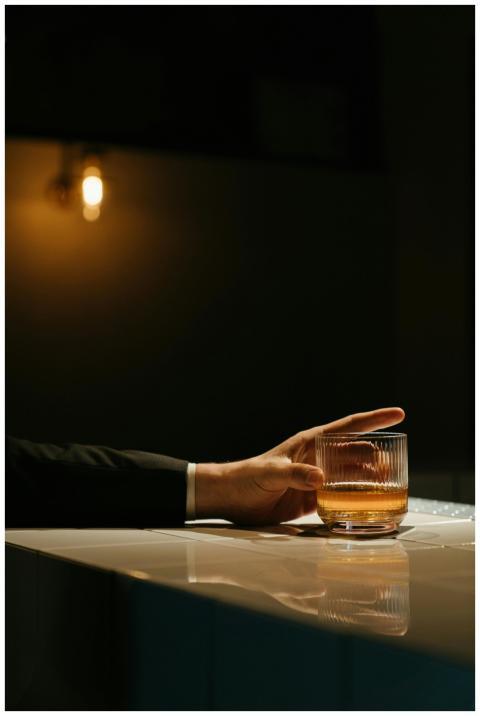 Hand holding a glass of whiskey on a bar counter,