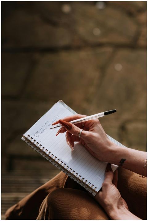 A woman's hand writing in a notebook outdoors, cap