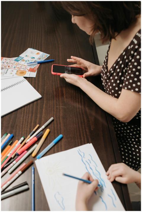 A mother supervises her child drawing at a table w