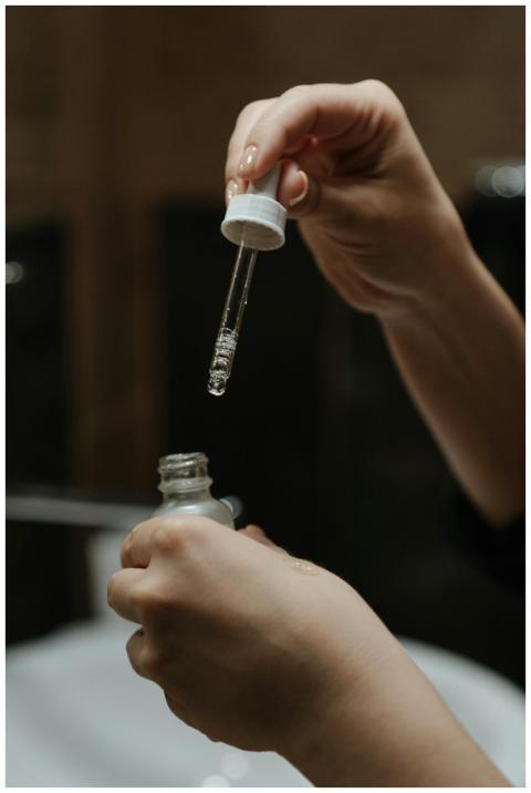 Hands holding a serum dropper applying skincare pr