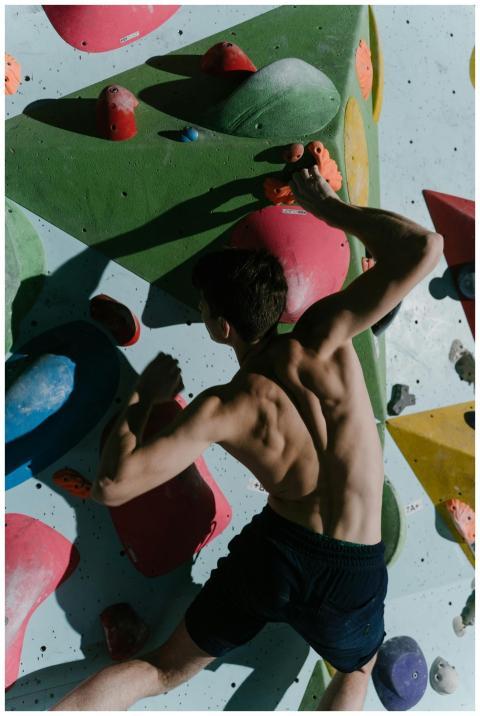 A muscular man engaging in indoor bouldering on a