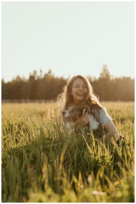 Smiling woman with her pet dog in a sunlit meadow