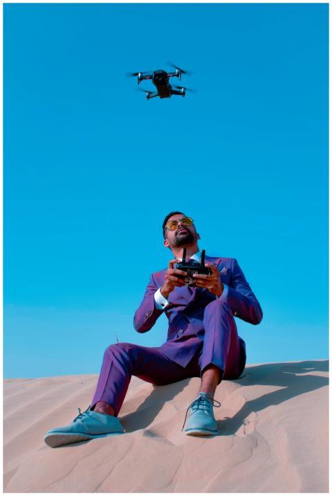 A stylish man in a purple suit controls a drone in