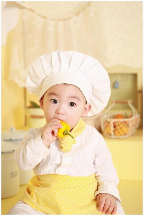 Cute baby in chef hat and apron nibbling a bell pe