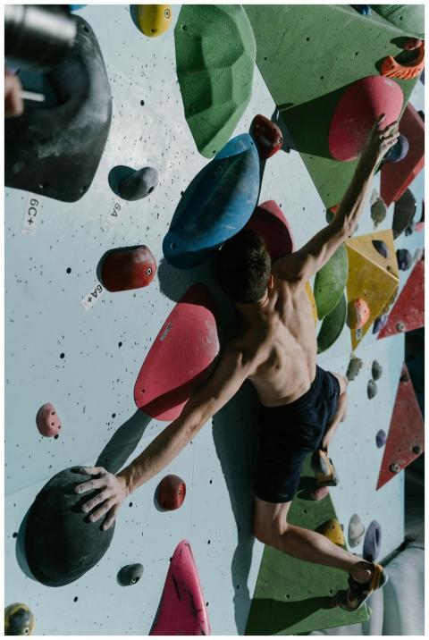 Shirtless male rock climber scales colorful indoor