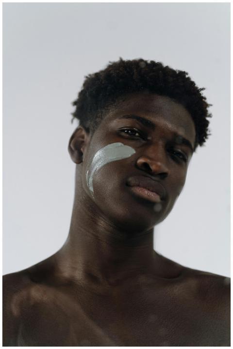 Close-up of a shirtless man with clay mask on chee