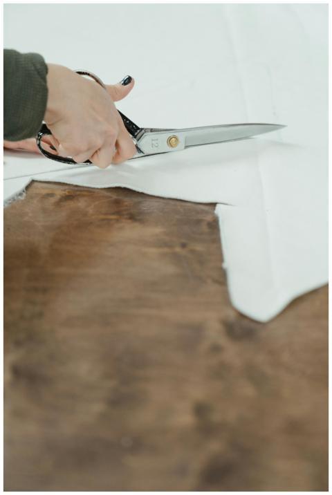 An artisan cuts white fabric on a wooden surface,