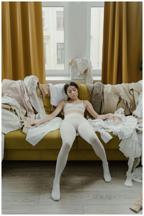 Woman lounging on couch surrounded by messy clothe