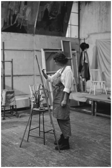 A woman artist in an apron painting on an easel in