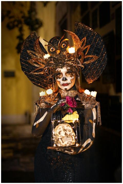 A woman in elaborate Day of the Dead makeup holds
