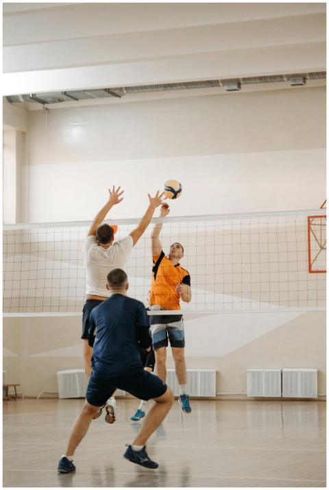 Three male athletes playing volleyball indoors, ca