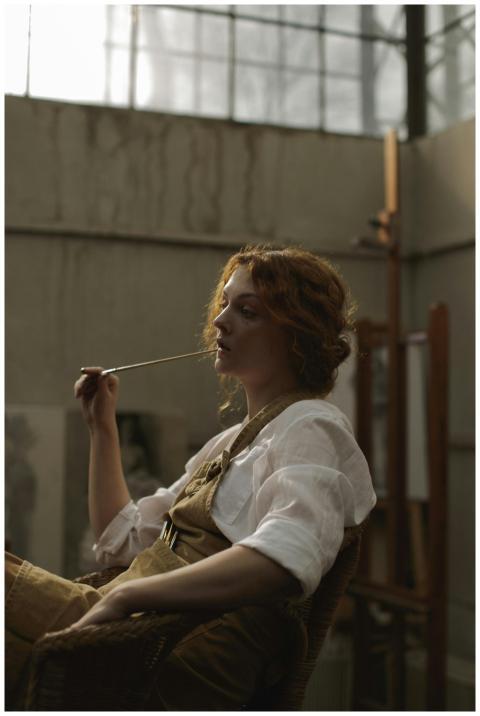 A woman artist in a studio deep in thought, holdin