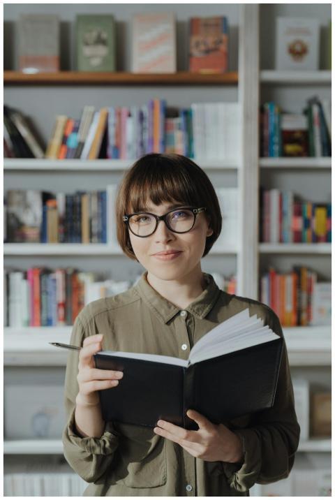Smiling woman in a library holding a book, surroun