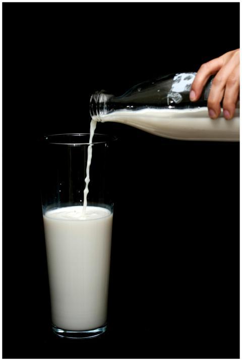 A hand pours fresh milk from a glass bottle into a