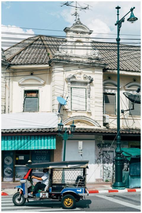 A tuk-tuk driving past vintage buildings on an urb