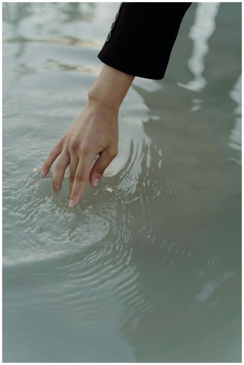 A hand elegantly touches the water surface creatin