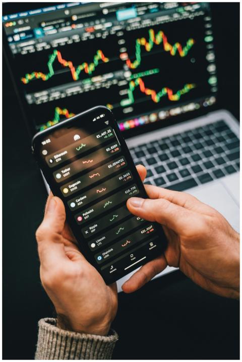 Hands holding smartphone with stock app, laptop di