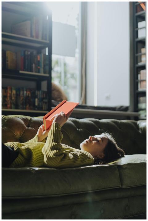 A young woman in a green sweater reads a book whil