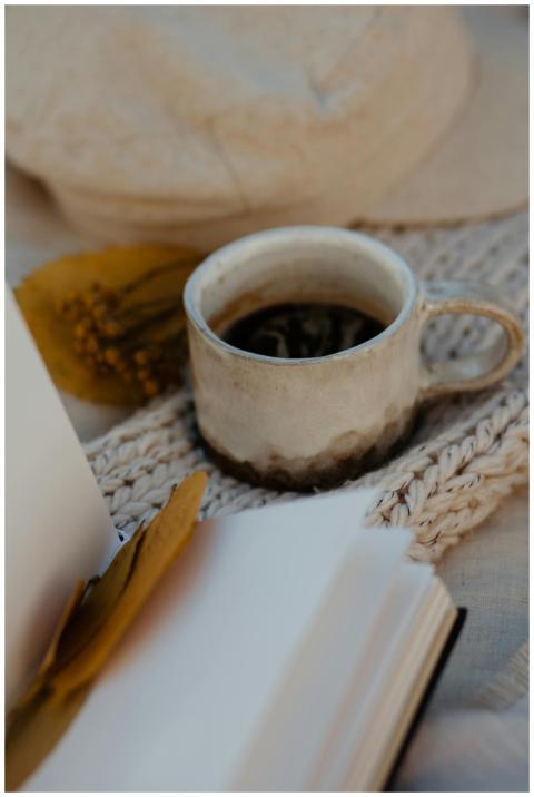 A rustic ceramic coffee cup sits beside an open bo