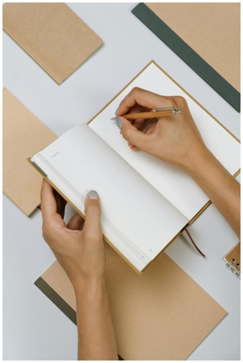 Top view of hands writing in an open notepad surro