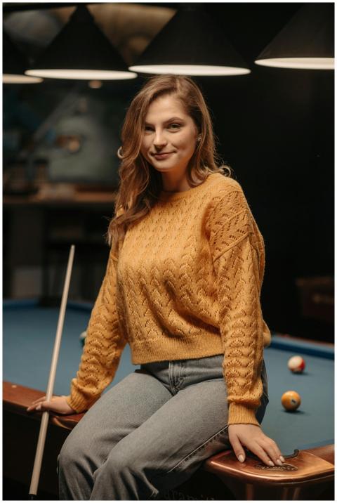 Woman sitting on a billiard table with a cue stick