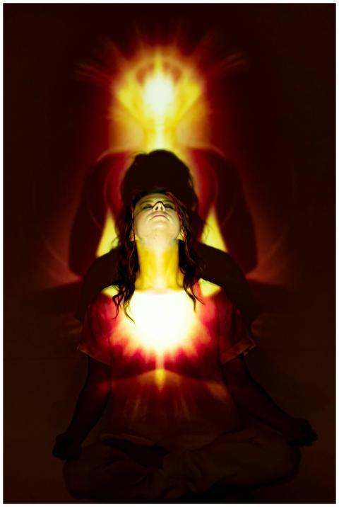 A woman meditates with a vibrant aura and light pr