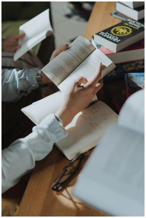 Person writing in a notebook while reading, surrou
