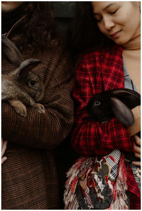 Two people in stylish coats holding rabbits, creat