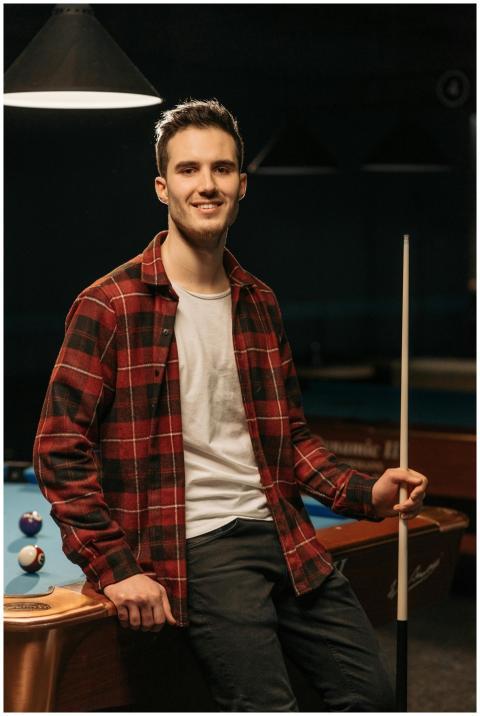 Smiling young man in flannel shirt poses with cue