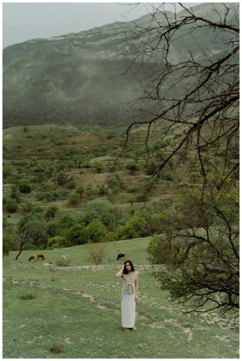 Woman standing in a lush, green mountain field sur