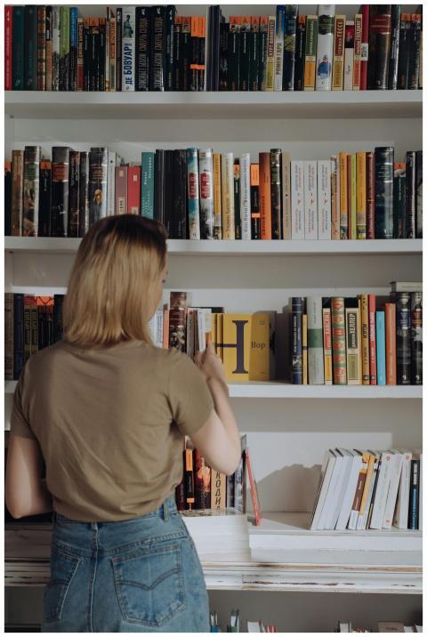 A young woman browses a library bookshelf, explori