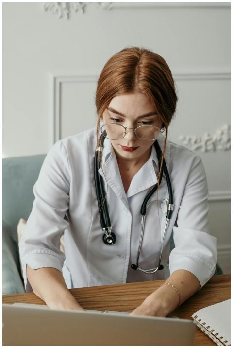 Focused female doctor using laptop in clinic, wear