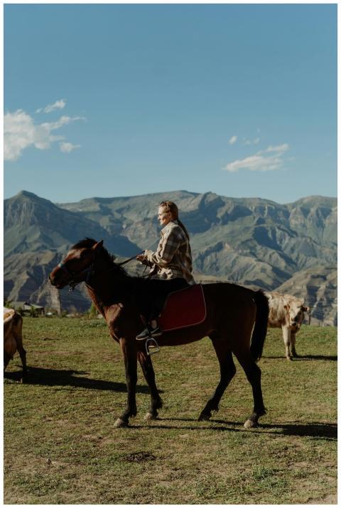 A woman rides a horse in a scenic mountainous coun