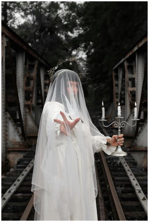 A veiled person holding a candelabra standing myst
