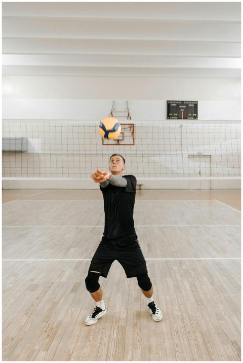 Man practicing volleyball indoors, preparing to hi