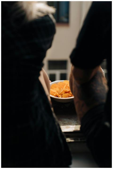 A bowl of potato chips on a table surrounded by pe