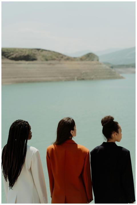 Three women in vibrant blazers stand by a scenic l