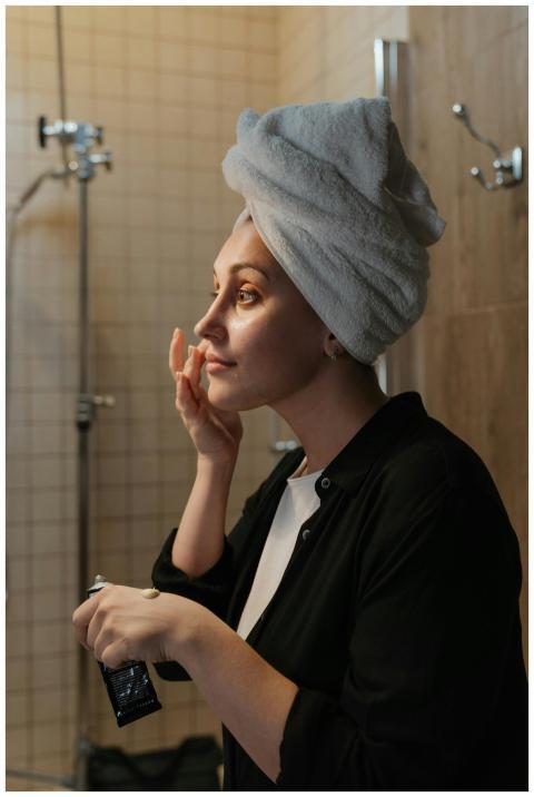 A woman in a towel applies skincare cream in her b