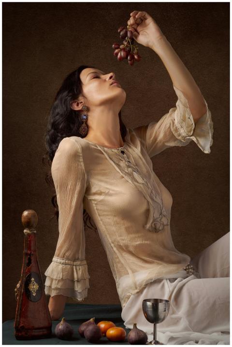 Stylish woman holding grapes in a vintage setting,