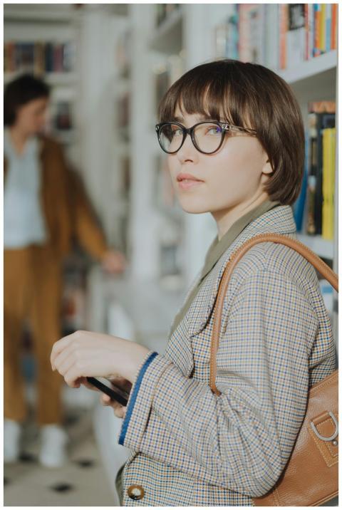 Stylish young woman with glasses browsing books in