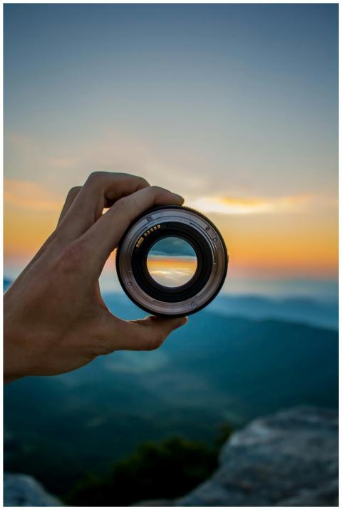 A hand holding a camera lens against a scenic suns