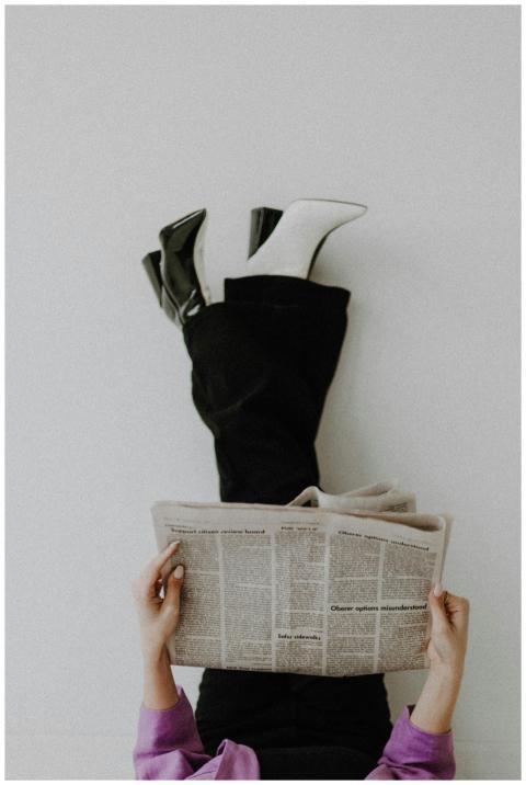 Fashionable woman reading newspaper with legs up a