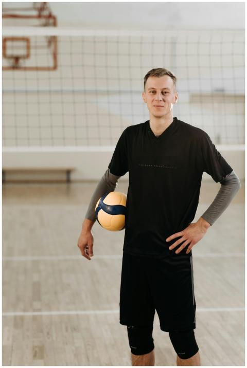 A male volleyball player posing with a ball in an