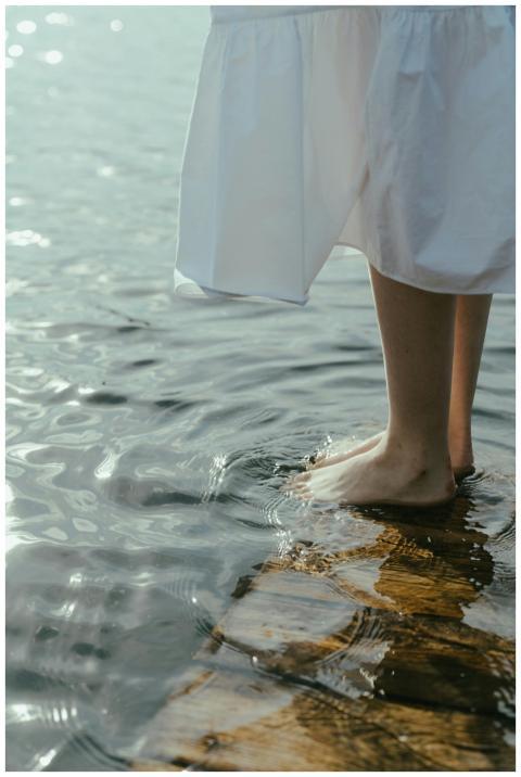 A woman in a white dress stands barefoot on a wood