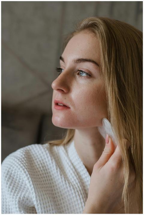 A woman using a gua sha tool for facial massage, p