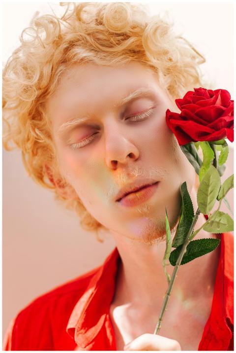 Close-up of a young albino man holding a red rose,