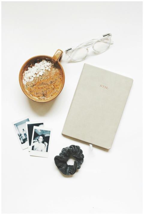 A cozy flatlay featuring a coffee, notebook, eyegl