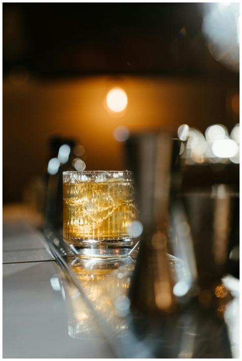 A glass of whiskey with ice on a reflective bar su