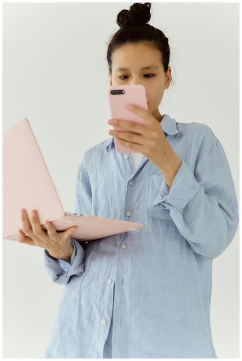 Woman in a blue shirt uses a smartphone and laptop
