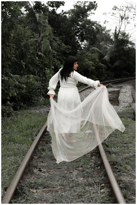 A woman in a flowing white dress walks along railr